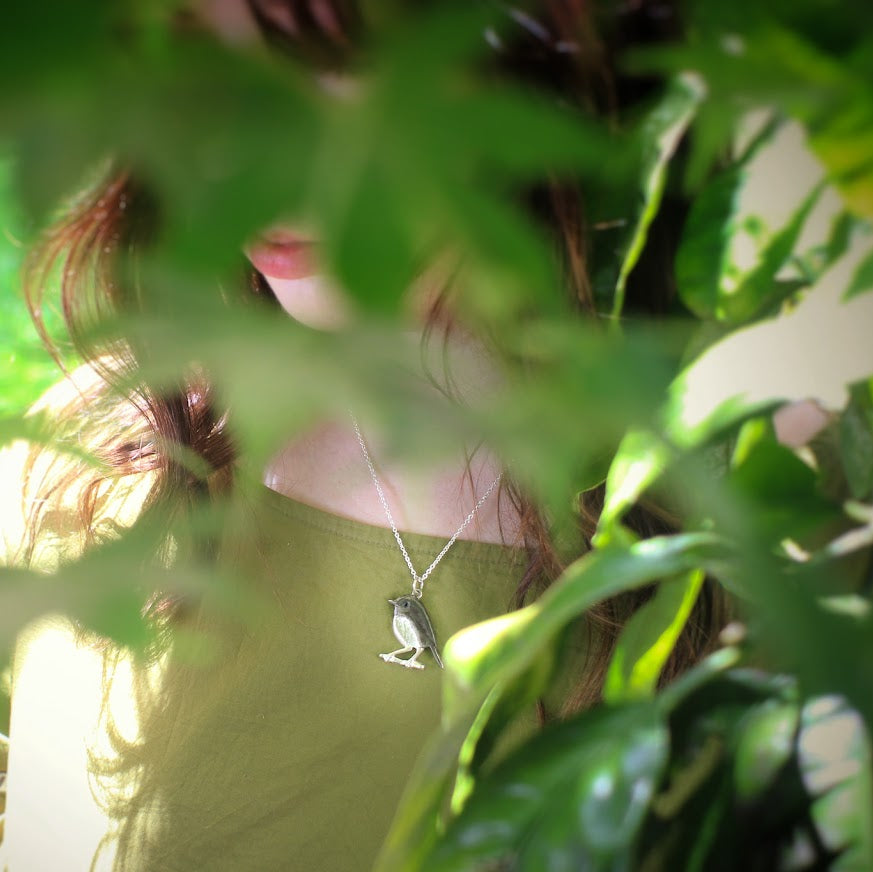 Person wearing a yellow top with floral patterns, partially obscured by green leaves.