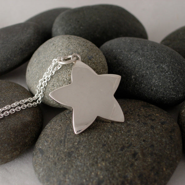 Silver star-shaped pendant on a chain lying on dark stones