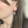 A close-up of a person's ear wearing a small dangling silver Fantail earring.