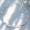 Silver necklace on a light blue background with tree shadows
