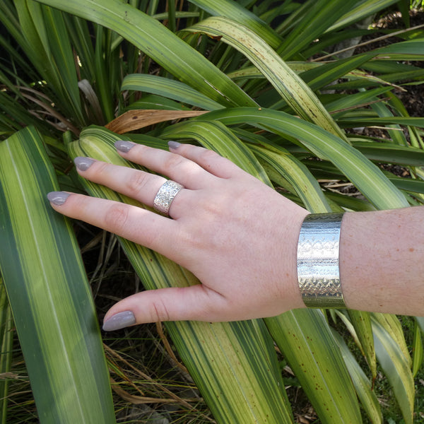 Photo of arm and hand wearing silver cuff bracelet and wide textured silver ring against flax background, handmade by Tania Mallow Jewellery